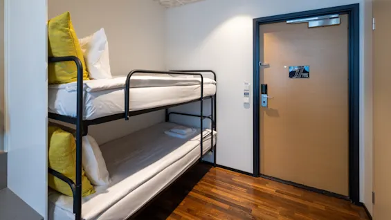 A cozy room featuring bunk beds with fresh white linens and bright pillows, next to a wooden door with the number 118.