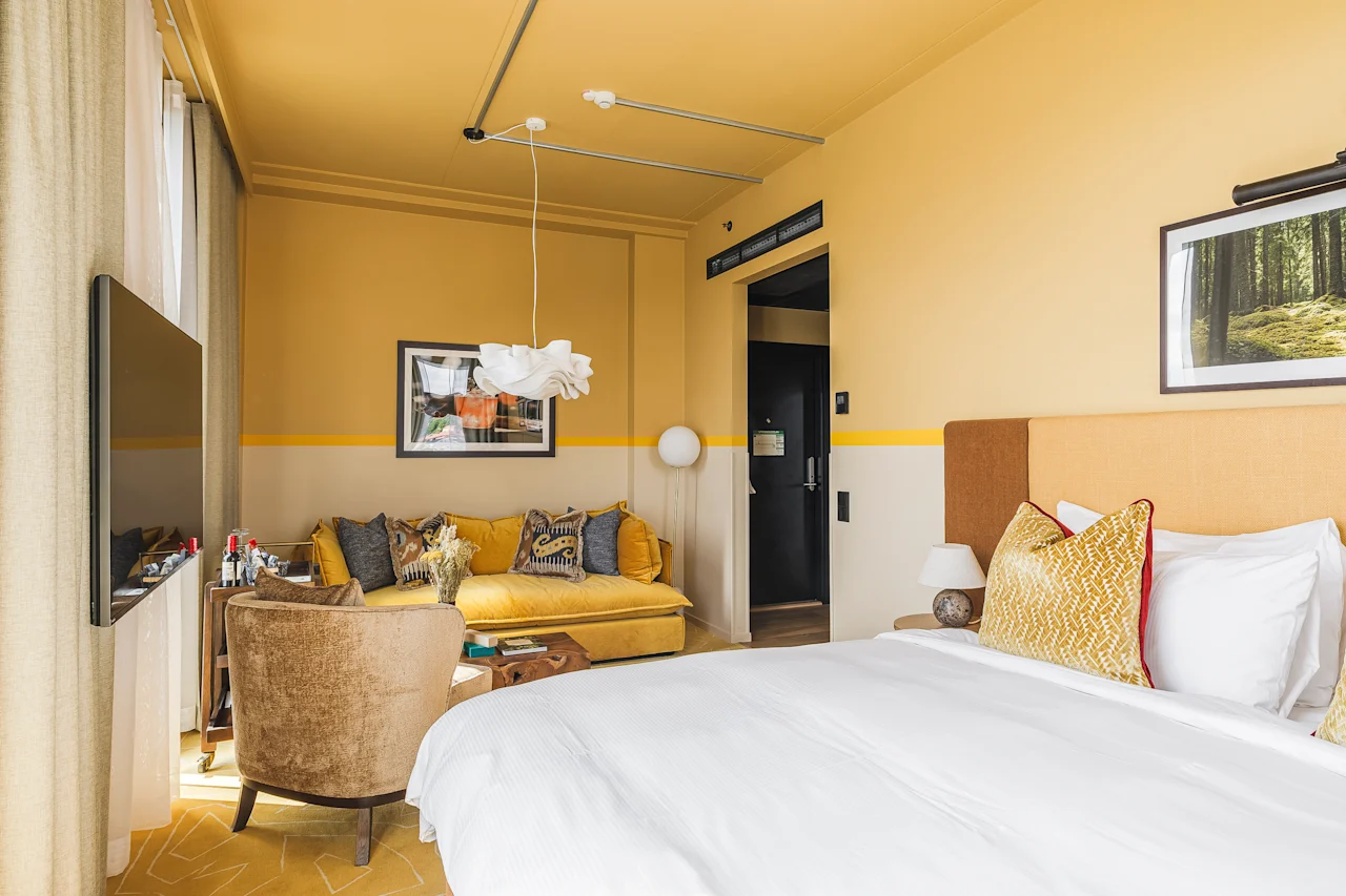 Et levende hotelværelse på Hernö Gin Hotel med en hyggelig seng, en komfortabel gul sofa og moderne indretning.