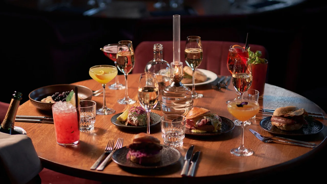 Et koselig bord på Clarion Hotel Post dekket med deilig mat, cocktails og vin, opplyst av en varm lampe.