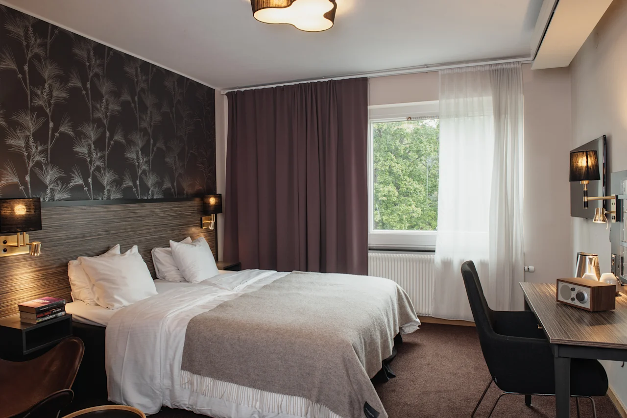 A serene hotel room with a comfortable bed, a dedicated workspace, and a window offering a peaceful view of nature.