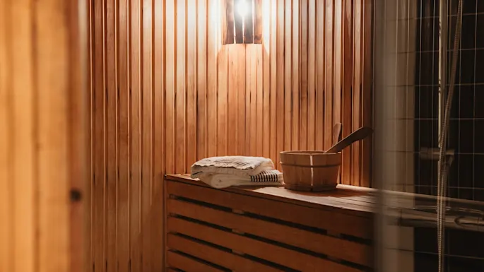 Home Hotel Kung Oscar badstueinteriør med varme trebenker, håndklær og en bøtte, klart for avslapning.