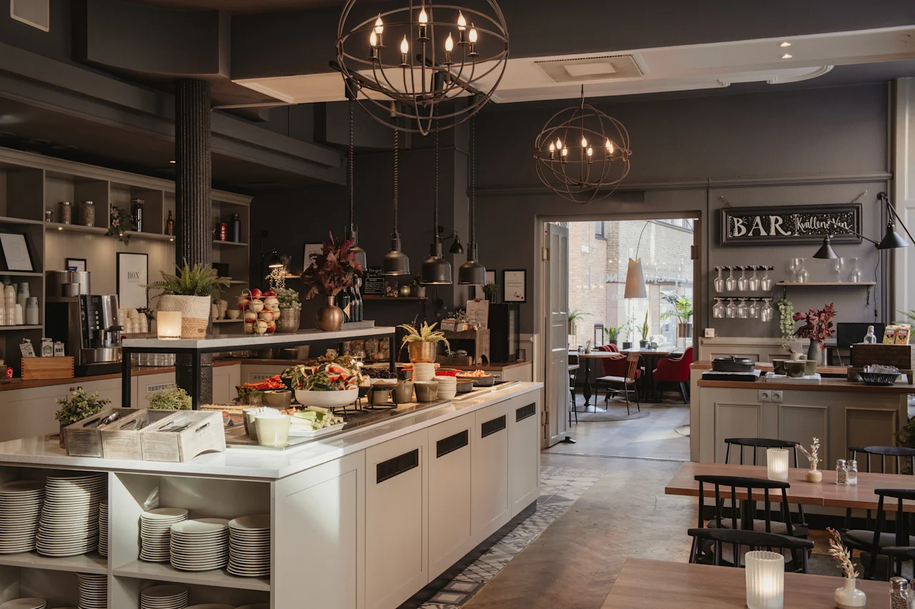 En velutstyrt hotellrestaurant med en buffé og et barområde. Bord er dekket for bespisning, noe som skaper en innbydende atmosfære.