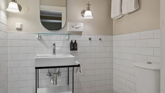 A clean and modern bathroom featuring a white tiled wall, a sink with a mirror, and a toilet with fresh towels.