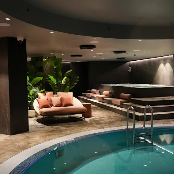 Modernt inomhus-spa på hotell med en rund turkos pool, bekväma lounge-sittplatser, dämpad belysning och gröna växter.