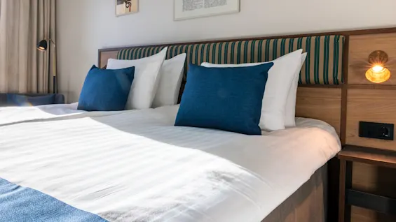 A comfortable hotel bed with white linens and blue accents, ready for a relaxing stay at Quality Hotel The Book in Gothenburg.