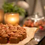 Sjokoladekaker er pent arrangert på bakepapir, omgitt av tente lys, en glassklokke og grønt på et trebord, som skaper en koselig, inviterende atmosfære.