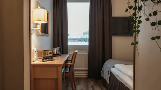 Ett bekvämt hotellrum med ett skrivbord med vattenkokare och radio, ett fönster och en mysig säng.
