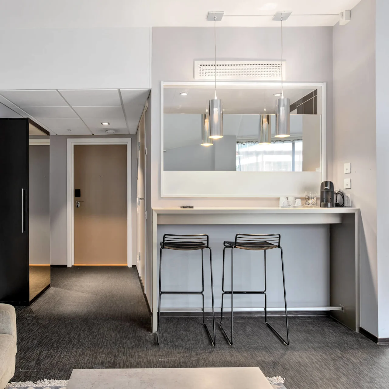 A modern hotel room with an open plan featuring a kitchenette, couch, and a glimpse of a bed, showcasing a clean and minimalist aesthetic.