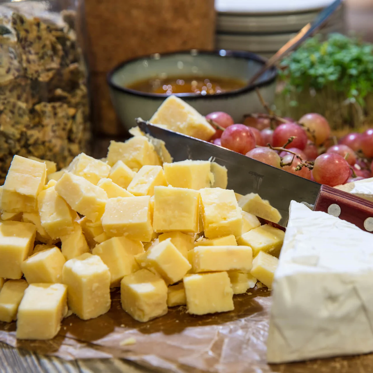 Various cheeses and grapes on a wooden board with a knife, suggesting a gourmet setting or cheese tasting event.