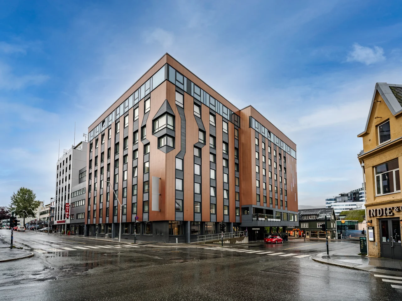 Moderni hotellirakennus puu- ja harmaalla julkisivulla märällä kaupungin kulmassa. 