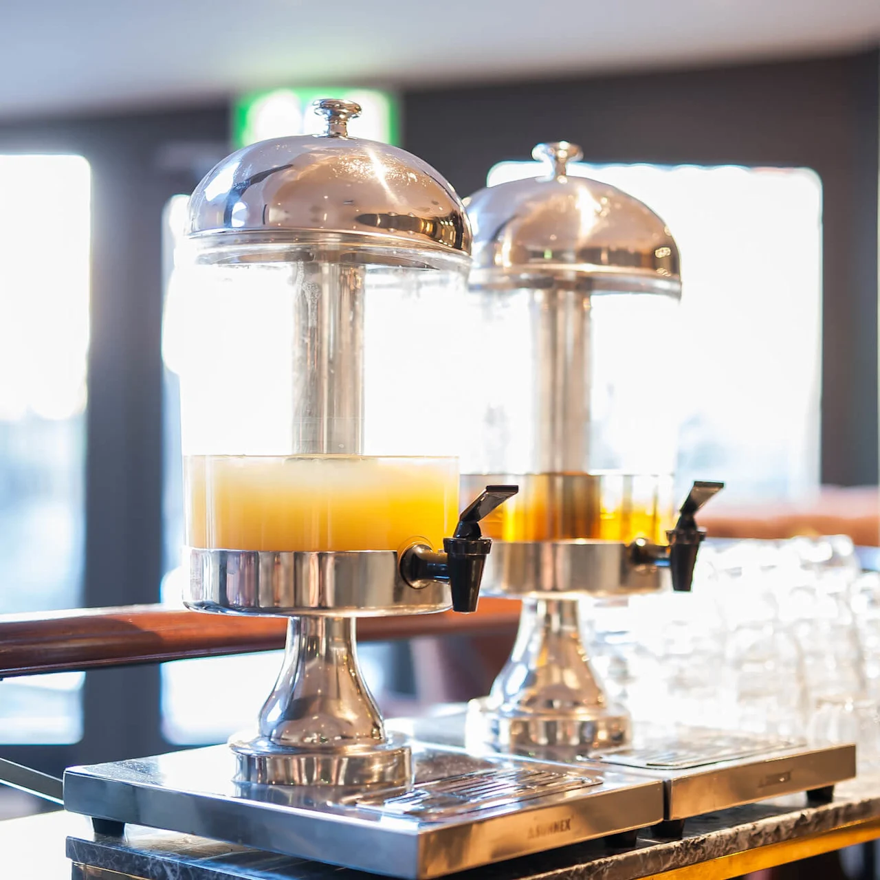 To drikkebeholderne med juice på en vogn, omgitt av glass i et lyst rom.