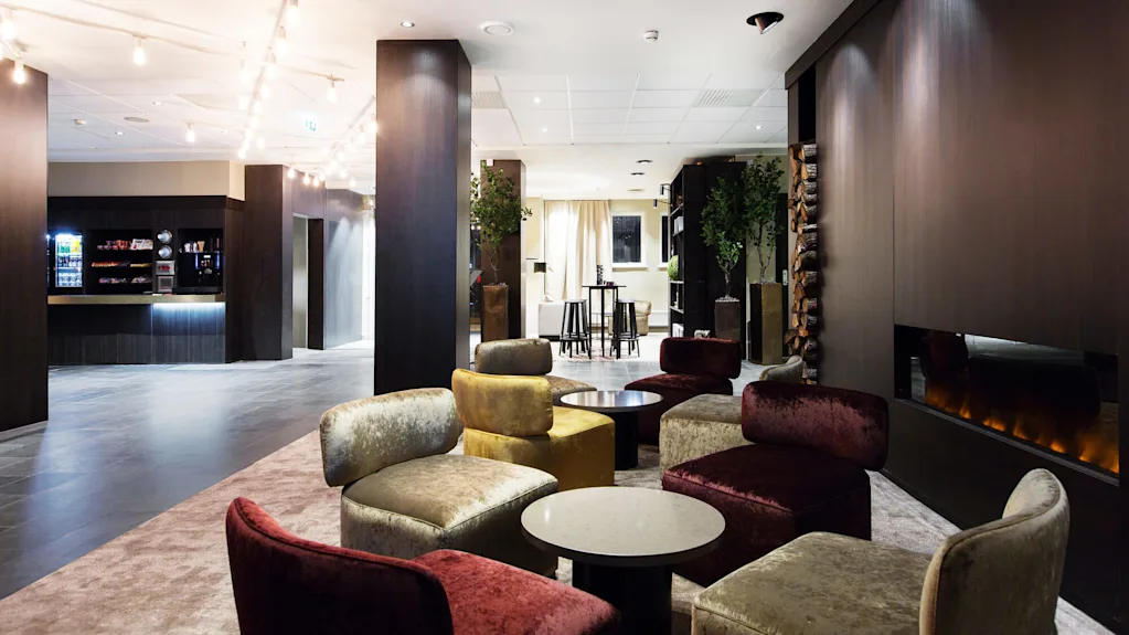 Luksuriøse sitteområder med komfortable stoler omgir bord ved siden av en elegant, moderne peis. Den romslige salongen har stemningsfull belysning og en snackbar i bakgrunnen.