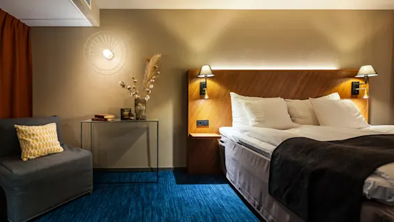 Ett snyggt bäddad säng med stämningsbelysning i ett modernt hotellrum, med varma färger och dekorativa detaljer.
