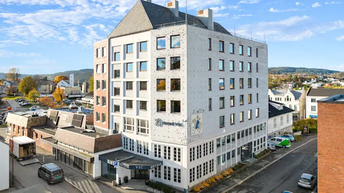 En lys hotelbygning i et urbant område under en blå himmel med lette skyer