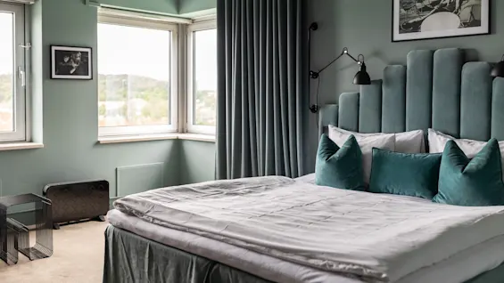 Et komfortabelt soverom med en stor seng, turkise detaljer og store vinduer som gir en lys og luftig atmosfære.