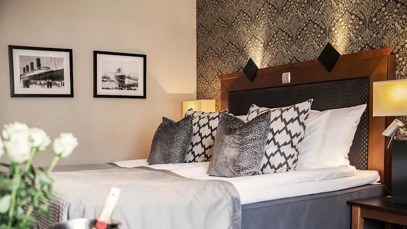 A neatly made bed with decorative pillows, framed pictures above, in a stylish bedroom. No text is visible.