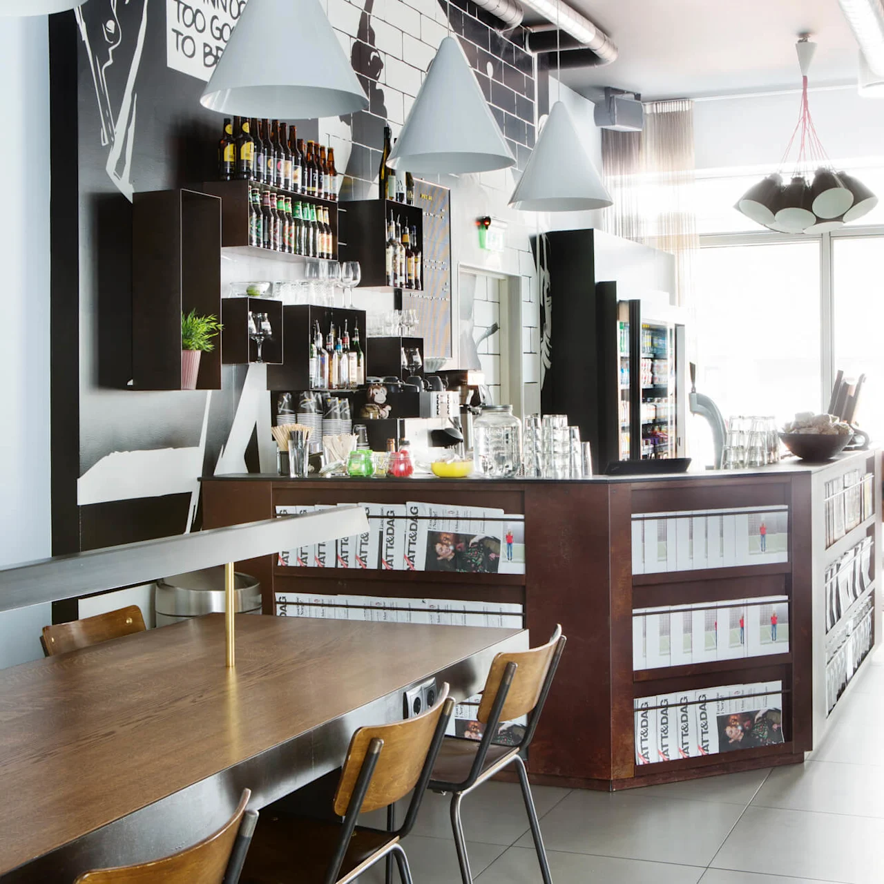 A modern café interior features a wooden counter with shelves of magazines, a wall with bottled drinks, and pendant lamps above. Natural light streams in through large windows. Text: “Innocent to Good to Be.”
