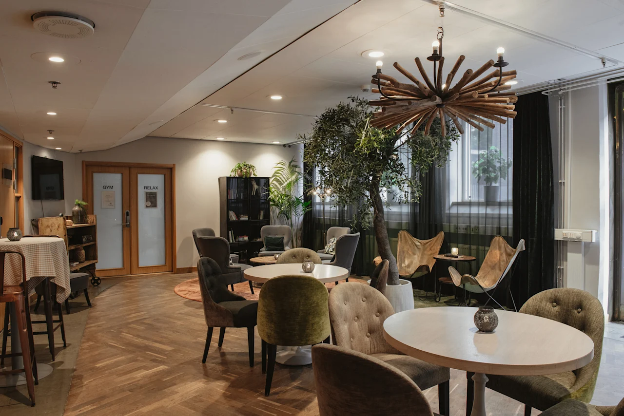 Home Hotel Uppsala: A cozy lounge area with various seating, a large plant, and doors labeled GYM and RELAX.
