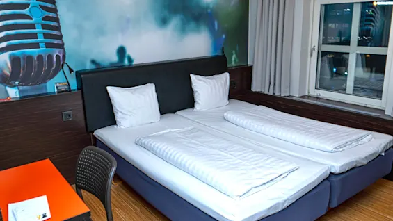 Ett hotellrum med två enkelsängar, en stor mikrofonmålning på väggen, ett fönster och ett skrivbord med en välkomstlapp.