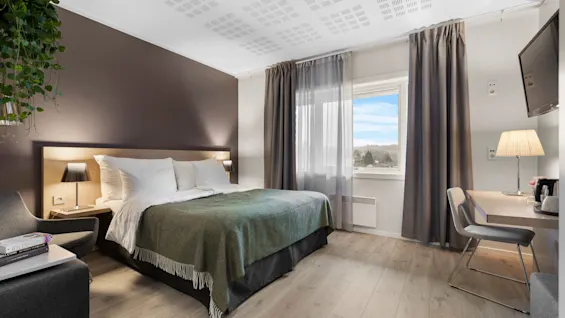 Et moderne og innbydende hotellrom med en komfortabel seng, et skrivebordsområde og et vindu med naturskjønn utsikt.