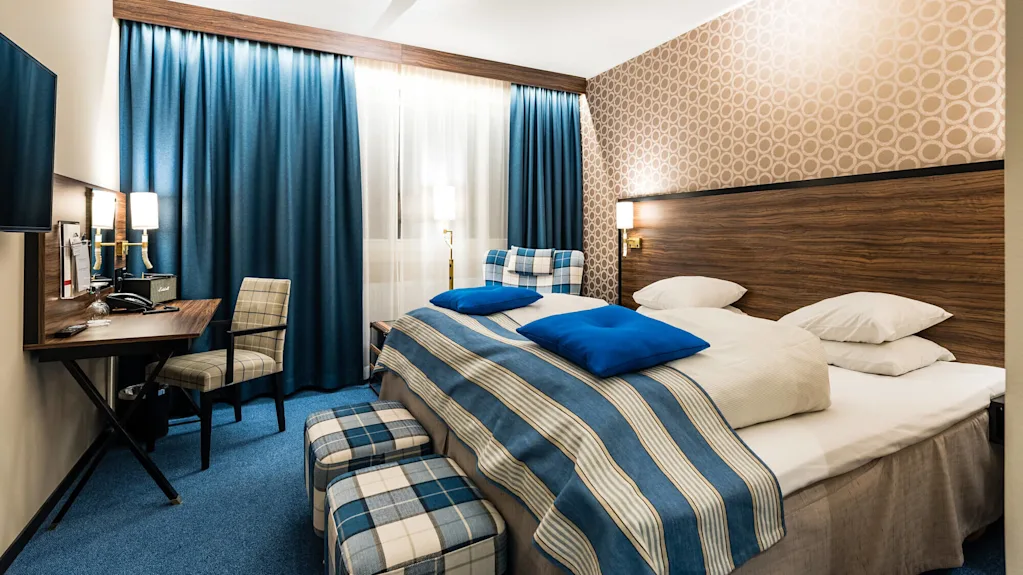 A neatly arranged hotel room with blue accents, patterned wallpaper, and a made bed, suggesting hospitality and comfort.