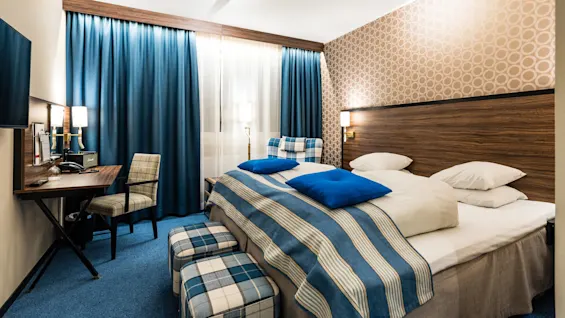 Ett snyggt ordnat hotellrum med blå accenter, mönstrad tapet och bäddad säng som antyder gästfrihet och komfort.