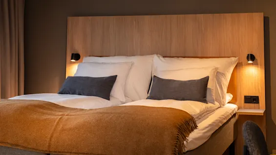 A comfortable bed in a modern hotel room, lit by warm bedside lamps, inviting a restful night's sleep.