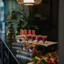 Kauniisti järjestetty catering-esillepano punaisilla shoteilla, marjaparfailla ja värikkäillä voileivillä tummalla pöydällä.