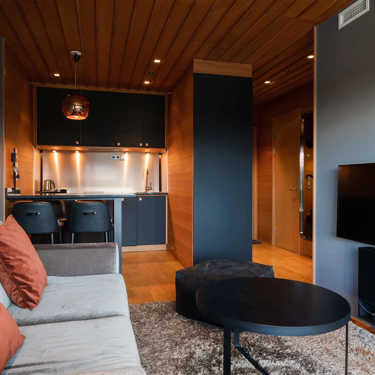 Modern living room with a sofa, kitchen counter, and TV; warm and cozy atmosphere with wooden accents.