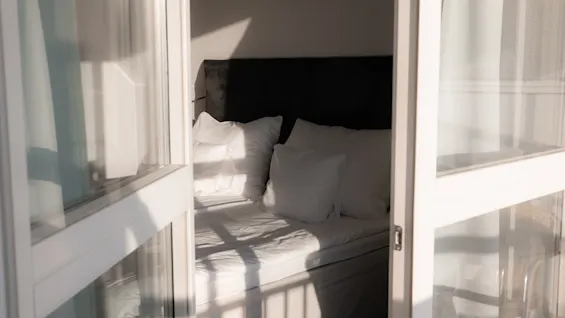 Solrigt soveværelse med en pænt redt seng, set gennem en åben dør, der inviterer til en fredelig start på dagen.