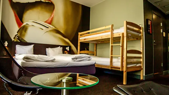 Ett livfullt hotellrum med en stor väggmålning av en sjungande person, med en dubbelsäng och en våningssäng i trä.