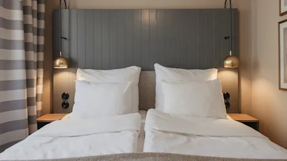 A cozy hotel room with a bed, white linens, and warm lighting from bedside lamps, inviting relaxation.