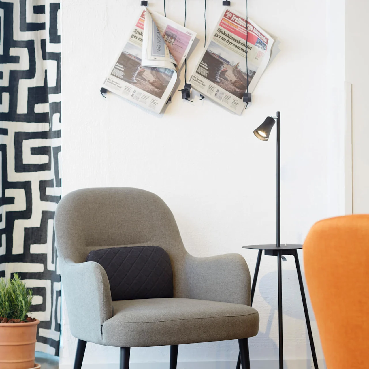 A modern armchair and a side table with a lamp, next to a wall-mounted magazine rack in a minimalist interior.