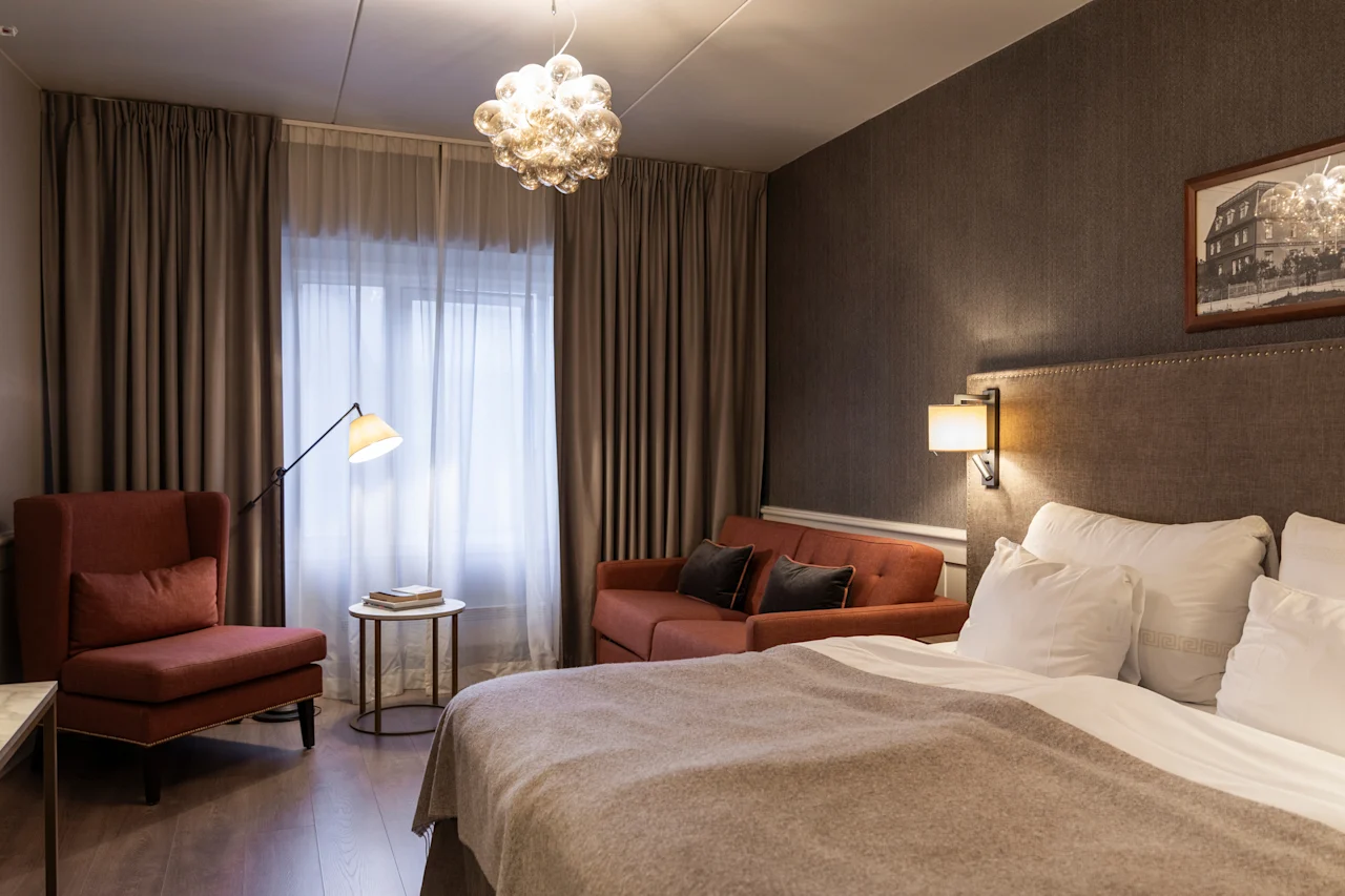 A welcoming hotel room at Home Hotel Grand Bodø featuring a comfortable bed, a sofa, and an armchair with warm lighting.