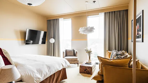 Et stilfuldt hotelværelse på Hernö Gin Hotel med en stor seng, en hyggelig sofa og lyse vinduer, designet til afslapning.