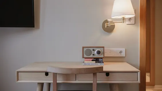 Et hyggeligt skrivebordsområde på Home Hotel Wellington, med et træskrivebord, stol, bøger og en radio, oplyst af en væglampe.