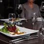 En hvit rektangulær tallerken med en salat av rødbeter, grønnsaker og ost står på et trebord. Rødvinsglass og vannglass er plassert rundt spiseplassen.