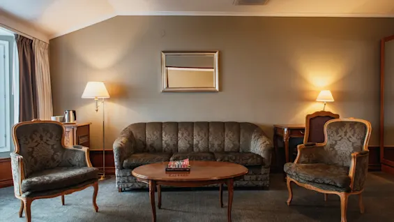 Ett mysigt hotellrum med klassiska möbler, inklusive en soffa, fåtöljer och ett soffbord, upplyst av varma lampor.