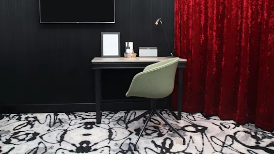 A modern workspace with a black desk, green chair, and dark wood paneling. A red velvet curtain adds color contrast. No visible text.
