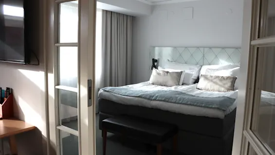 Bright hotel room with a double bed seen through glass sliding doors