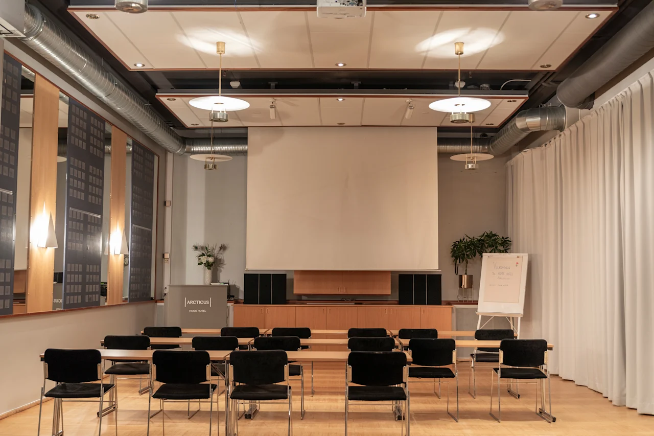 A modern conference room with rows of tables and chairs facing a large projection screen, ready for a presentation.