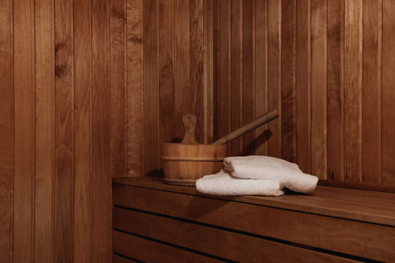 A cozy sauna interior with wooden walls and benches, featuring a bucket, ladle, and fresh white towels. Home Hotel Uppsala.