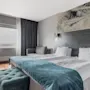 A comfortable hotel room with two beds, a cozy blue throw, and a window offering natural light. Perfect for relaxation.