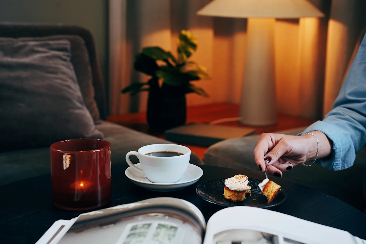 En person som koser seg med kaffe og kake i en koselig stue med tent lys.