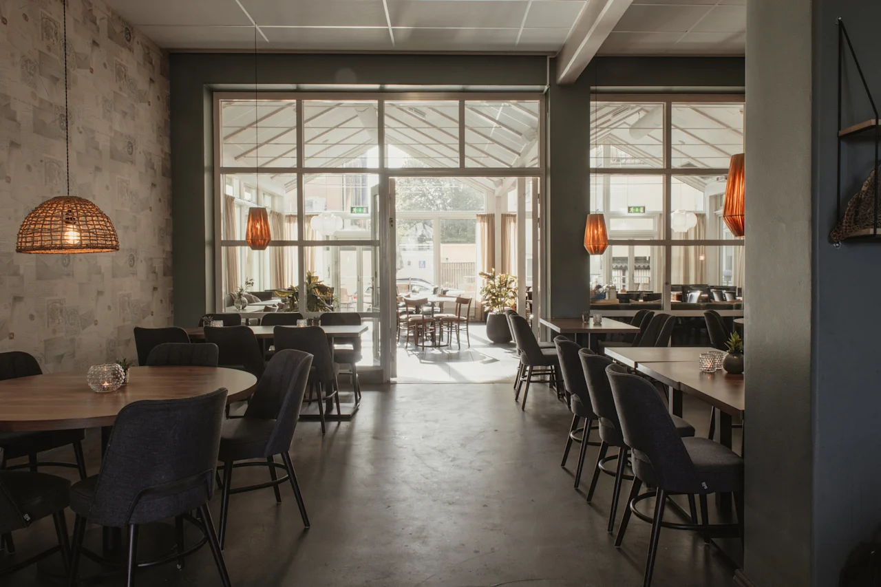 En ljus och inbjudande hotellrestaurang med moderna möbler, som leder till en uteplats genom stora glasdörrar. EXIT-skyltar synliga.