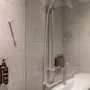 Et moderne bad med grå fliser, en dusj og en vask. To pumpeflasker merket BODY WASH og BODY LOTION er montert på veggen.