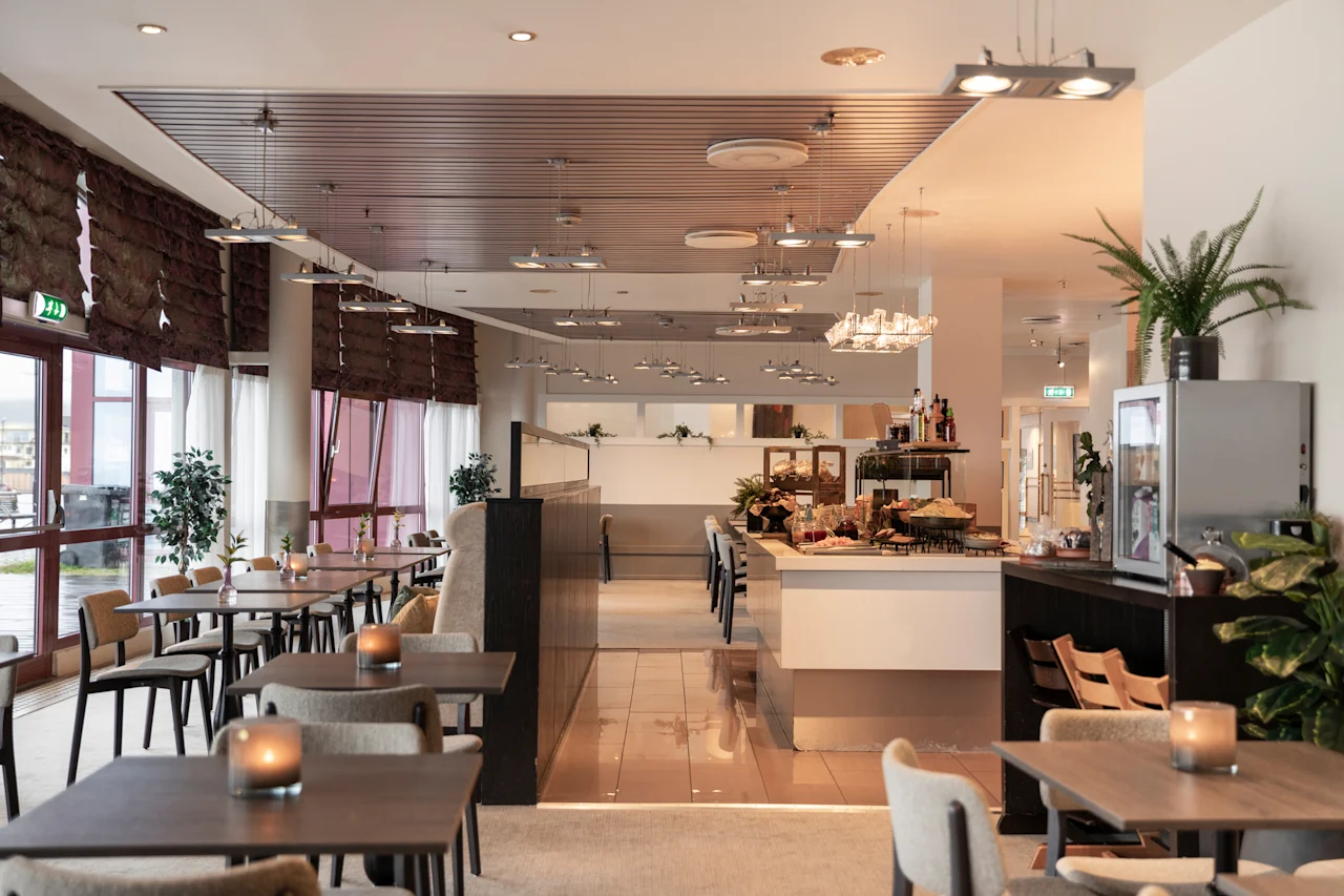 Kutsuva hotelliravintola, jossa on katetut pöydät, mukavat istuimet ja buffet-alue, kylpee luonnonvalossa. Poistumiskyltti on näkyvissä.