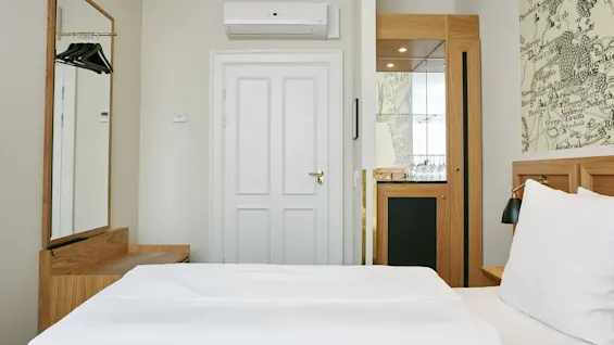 Et hyggeligt hotelværelse med en komfortabel seng, et helkropsspejl og et minibarområde, klar til en gæsts ophold.