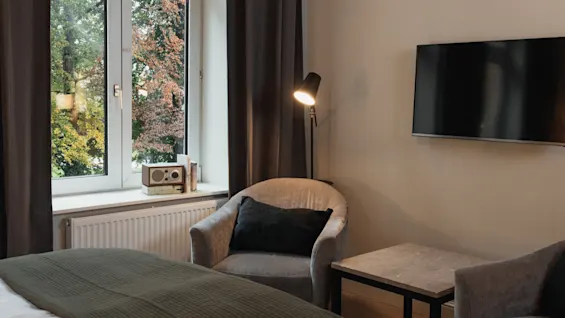 Et hyggeligt hotelværelse på Home Hotel Norre Park med en seng, lænestol, TV og et vindue med udsigt over efterårstræer.