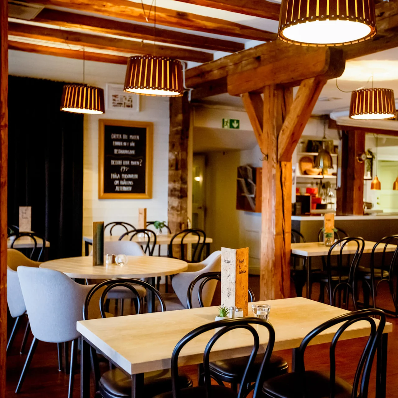 Wooden tables and chairs set in an inviting, rustic restaurant with warm lighting and timber beams.